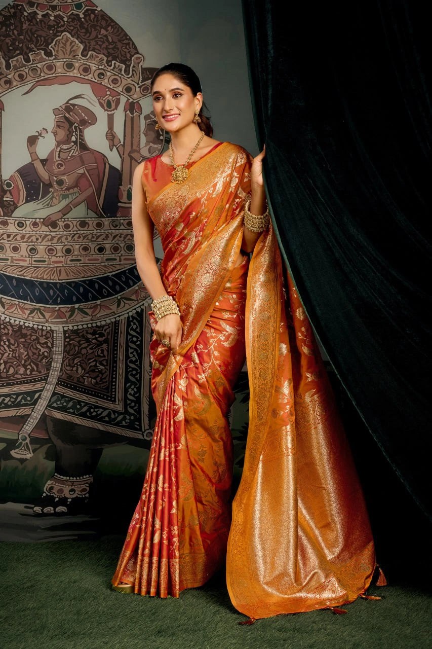 Woman in a traditional orange saree standing in front of an ornate backdrop